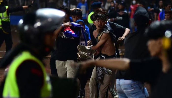 Young men run as police fire tear gas triggering a stampede at the Indonesian football stadium on Saturday night. — AFP