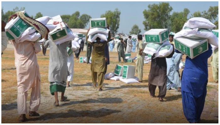 Flood-affected people carry relief packages received under the KSRelief programme. — APP