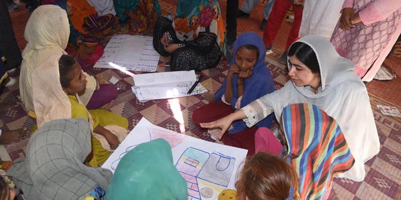 This handout picture taken and released by Chief Minister House Office of Sindh Province on October 12, 2022 shows Nobel Peace laureate Malala Yousafzai (R) speaking with flood-affected children at a makeshift school in Johi, Dadu district of Sindh province. — AFP