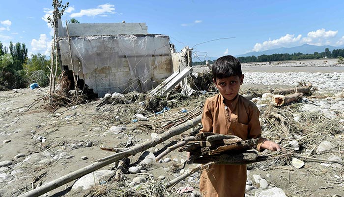 A boy carries wood near a damaged house along a river following heavy monsoon rains in Mingora, a town in Pakistan´s northern Swat valley on August 28, 2022. — AFP