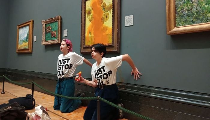 A handout picture from the Just Stop Oil climate campaign group shows activists with their hands glued to the wall under Vincent van Gogh´s Sunflowers after throwing tomato soup on the painting at the National Gallery in central London on October 14, 2022.— AFP