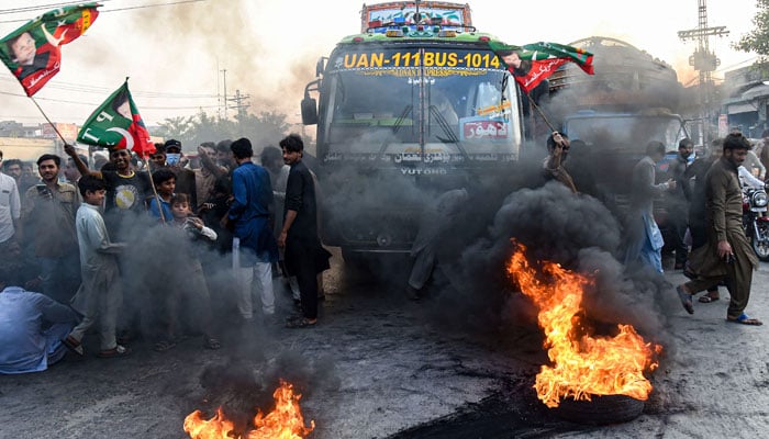 Activists of PTI party shout slogans infront of burning tyres against the disqualified decision of former prime minister Imran Khan along a street in Lahore on October 21, 2022. — AFP