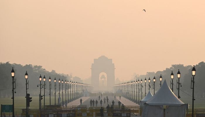 People walk along a road near India Gate amid smoggy conditions in New Delhi on October 25, 2022.— AFP