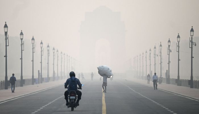 A man carries a sack along the road in front of India Gate amid smoggy conditions in New Delhi on November 1, 2022.— AFP