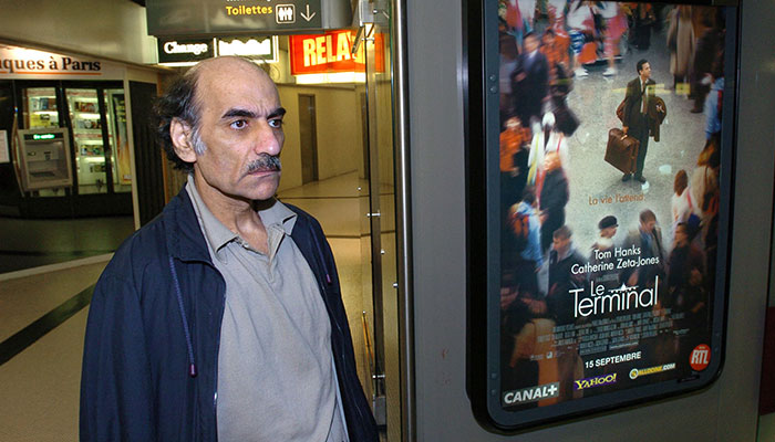 In this file photo taken on August 12, 2004, Mehran Karimi Nasseri passes by the poster of the movie inspired by his life, in terminal 1 of Paris Charles De Gaulle airport. — AFP