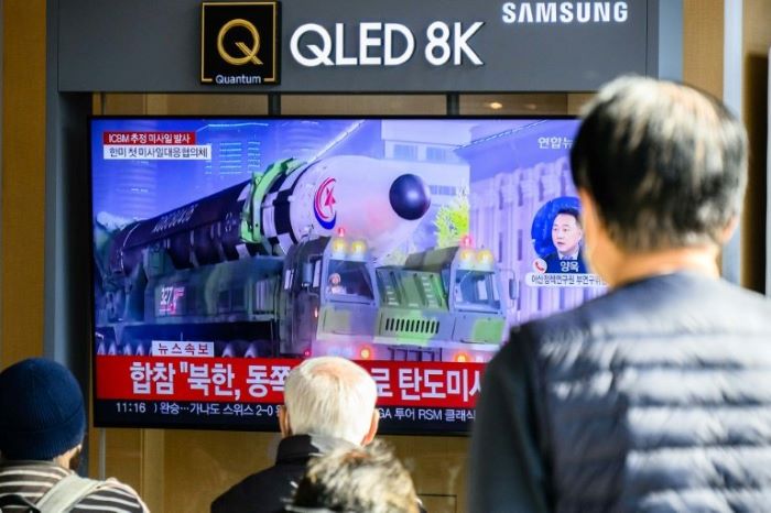 İnsanlar, Seul'deki bir tren istasyonunda, bir askeri geçit töreni sırasında sergilenen bir Kuzey Kore kıtalararası balistik füzesinin bir dosya fotoğrafının yer aldığı bir haber yayınını gösteren bir televizyonun yanında oturuyor.  - AFP
