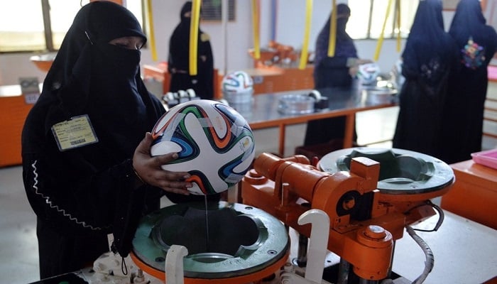 A worker applies adhesives to the edges of a design on a football ahead of the FIFA World Cup 2014 in Brazil at a factory in Sialkot. - AFP