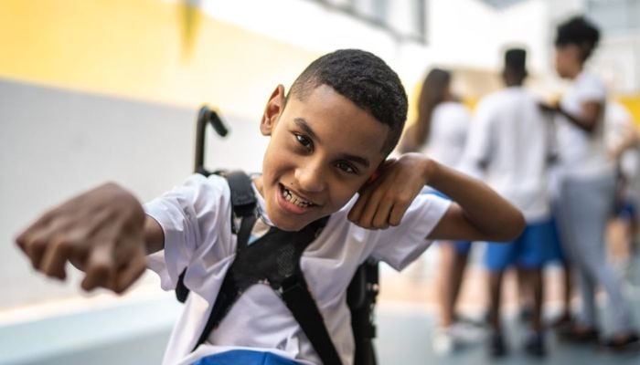 Bir spor sahasında Brezilyalı bir öğrencinin portresi.  Beyaz gömlek ve mavi şort giyen tekerlekli sandalye kullanıcısıdır.  —UNICEF