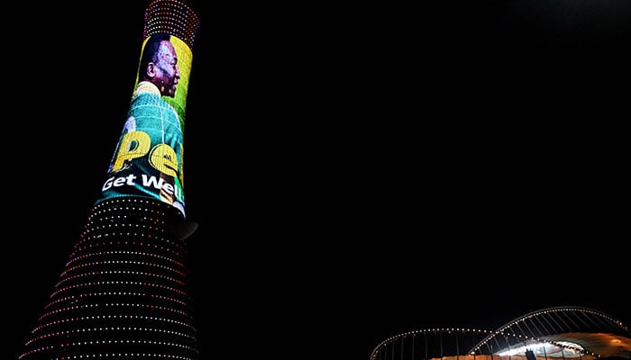 A picture taken on December 3, 2022, in Doha, during the Qatar 2022 World Cup football tournament, shows the Torch tower of Doha also knows as the Aspire Tower, lighten up by a screen depicting Brazilian star Pele and reading a message in support to the former Brazilian football player who is being treated for a respiratory infection at the hospital in Sao Paulo.