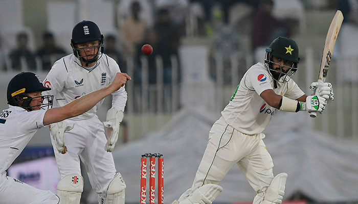 Pakistanlı Saud Shakeel (sağda), 4 Aralık 2022'de Rawalpindi'deki Rawalpindi Kriket Stadyumu'nda Pakistan ile İngiltere arasındaki ilk kriket Testi maçının dördüncü gününde İngiltere'nin kalecisi Ollie Pope (2L) izlerken şut atıyor. — AFP