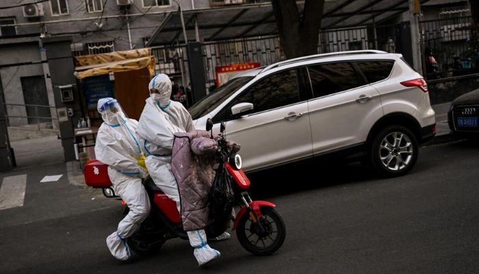 Health workers wearing protective equipment (PPE) ride a scooter near a residential area under lockdown.— AFP
