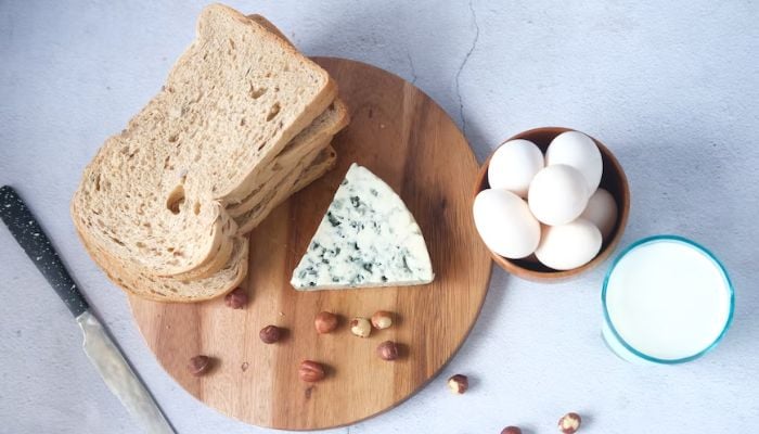 Pane, formaggio a fette, uova e un bicchiere di latte su un tavolo.  — Unsplash
