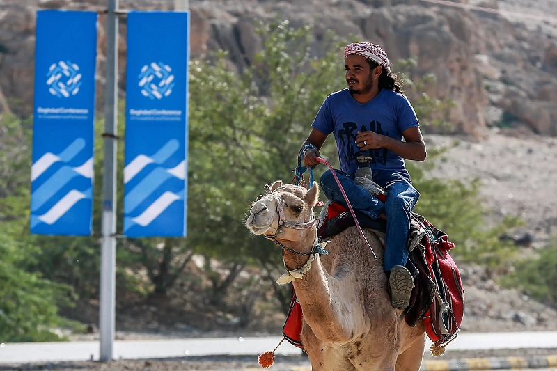 A man rides a camel along a road past signs bearing the name and logo of the Baghdad Conference for Cooperation and Partnership in Jordan.— AFP
