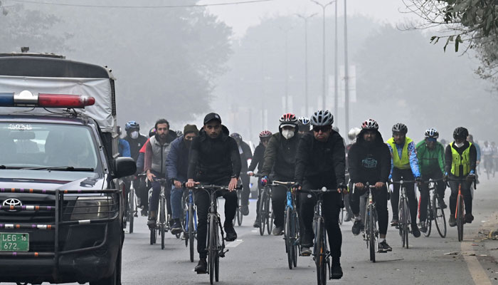 Bisikletçiler, 25 Aralık 2022'de Lahor'da Wagah sınırına doğru bir caddede bisiklet sürerken bir kirlilik ve sis bilinçlendirme kampanyasına katılıyor. — AFP