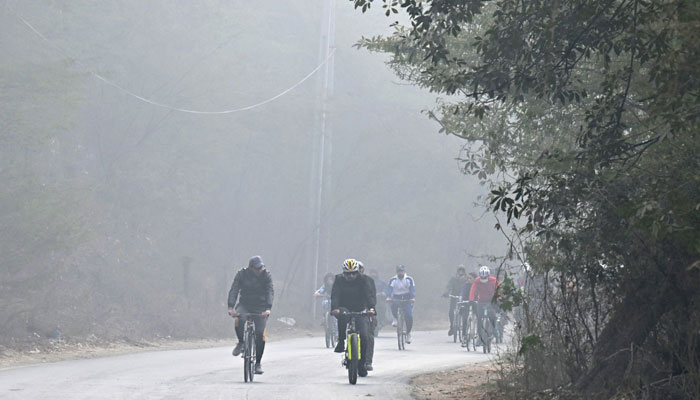 Bisikletçiler, 25 Aralık 2022'de Lahor'da Wagah sınırına doğru bir caddede bisiklet sürerken bir kirlilik ve sis bilinçlendirme kampanyasına katılıyor. — AFP