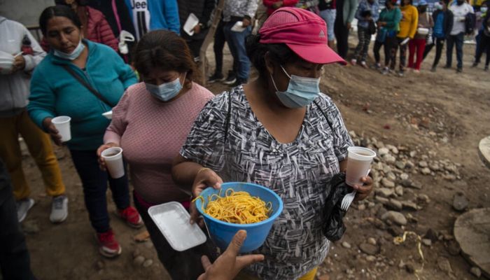 People queue for food at a soup kitchen in Peru.— AFP