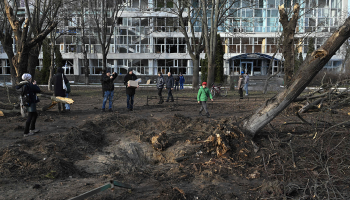 Görgü tanıkları, 1 Ocak 2023'te Kiev'deki bir eğitim binasının yanındaki kratere bakıyor. — AFP
