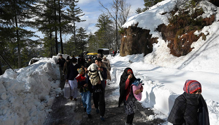 Tourists walk along a snow-covered road following a blizzard that started on January 7 which led to visitors being trapped in vehicles along the roads to the resort hill town of Murree, some 70km northeast of Islamabad on January 9, 2022. — AFP