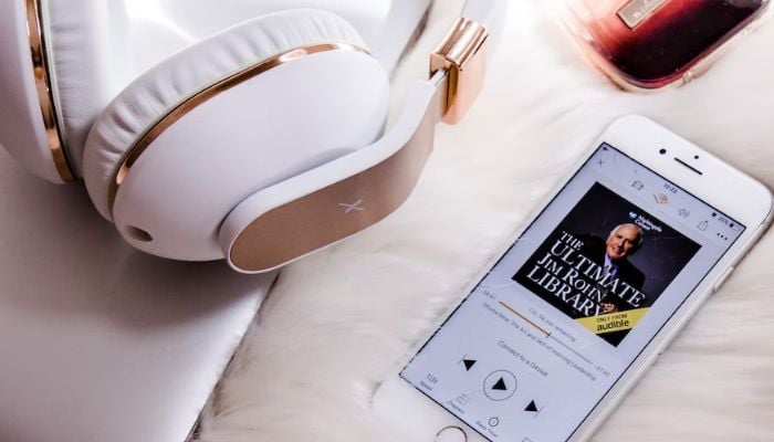 Image shows an audiobook on an iPhone with white headsets.— Unsplash