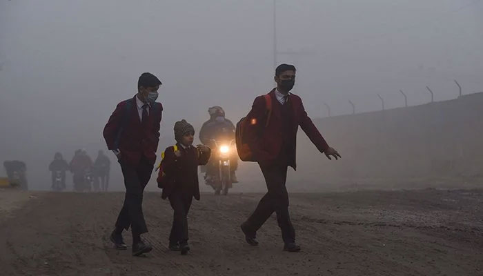 Children walk to their school along a street amid smoggy conditions early in the morning in Lahore on December 17, 2021. — AFP