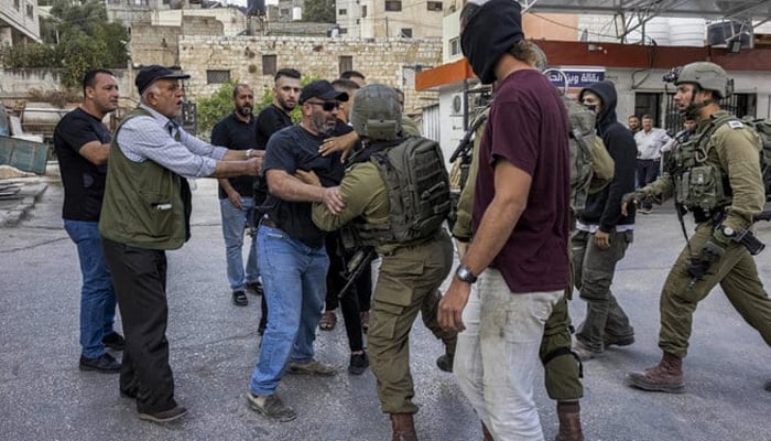 Israeli soldiers clash with Palestinians as a masked Israeli settler stands by in occupied West Bank. — AFP/File