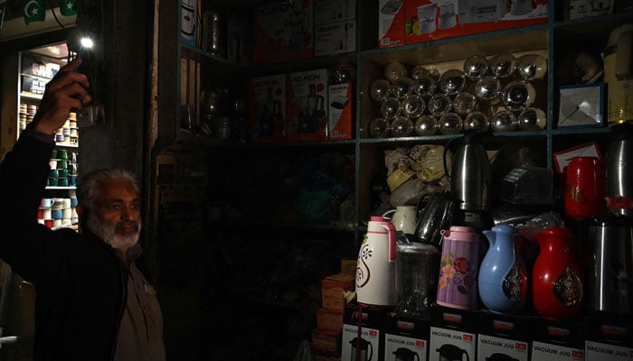 A shopkeeper uses his mobile phone´s torch light at a market during a nationwide power outage in Rawalpindi on January 23, 2023. — AFP