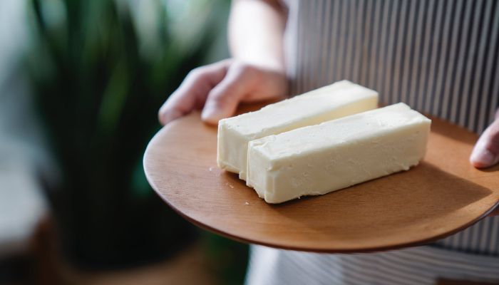 Close-up shot of a person holding a wooden plate with sliced margarine.— Pexels