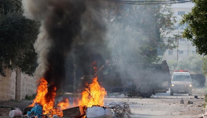 An ambulance drives past an Israeli military vehicle near a burning street barricade in the ocupied West Bank city of Jenin on January 26, 2023.— AFP