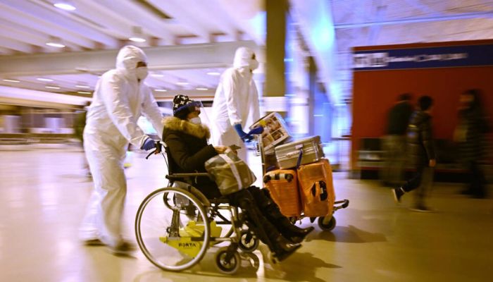 I lavoratori che indossano maschere e tute protettive aiutano un viaggiatore cinese a lasciare la sala arrivi dell'aeroporto internazionale di Roma Fiumicino il 29 dicembre 2022 dopo essere stato testato per COVID.— AFP
