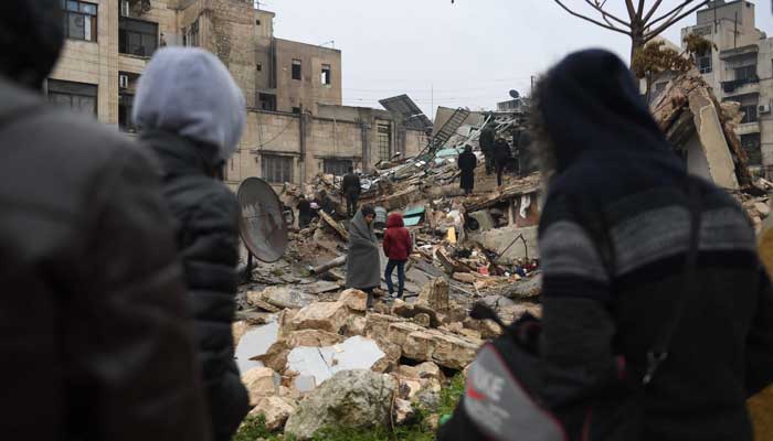 People gather around collapsed buildings as rescue teams look for survivors following an earthquake in the government-held Syrian city of Aleppo on February 6, 2023. — AFP