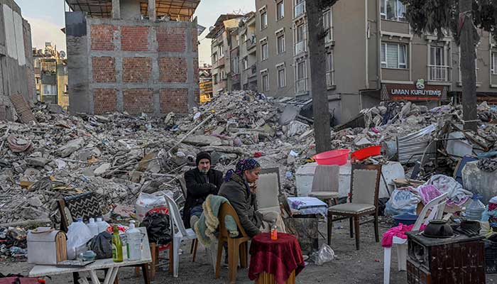 15 Şubat'ta Hatay'da depremin vurduğu yerinden edilmiş sakinler eşyalarıyla birlikte çöken binaların yanında oturuyorlar. — AFP