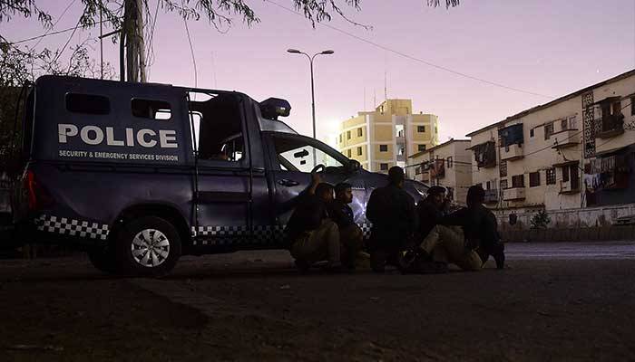 Güvenlik personeli, 17 Şubat 2023'te Karaçi'de bir polis yerleşkesine düzenlenen saldırının olduğu yerin yakınında bir polis aracının arkasında pozisyon alıyor. — AFP