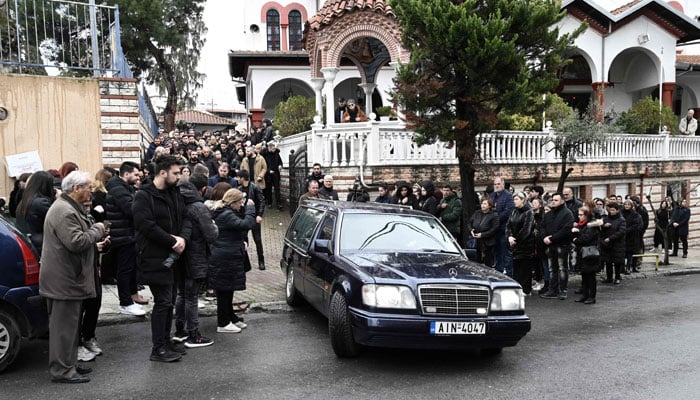 Katılımcılar, 4 Mart 2023'te Yunanistan'ın kuzeyindeki Giannitsa'da 23 yaşındaki Ifigenia Mitska'nın cenaze töreni sırasında geçen bir cenaze arabasına bakıyor. AFP