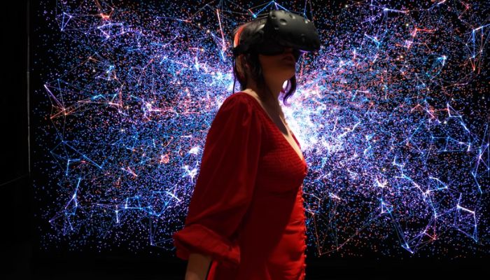 L'illustrazione mostra una donna che indossa un visore VR con una galassia sullo sfondo.— Unsplash