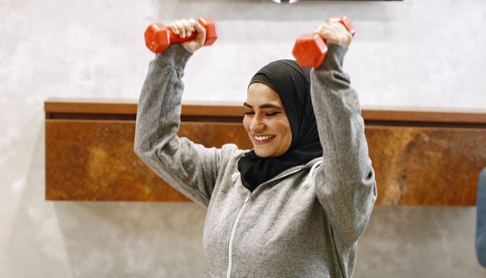 Donna in hijab durante l'allenamento con i manubri.— Pexels