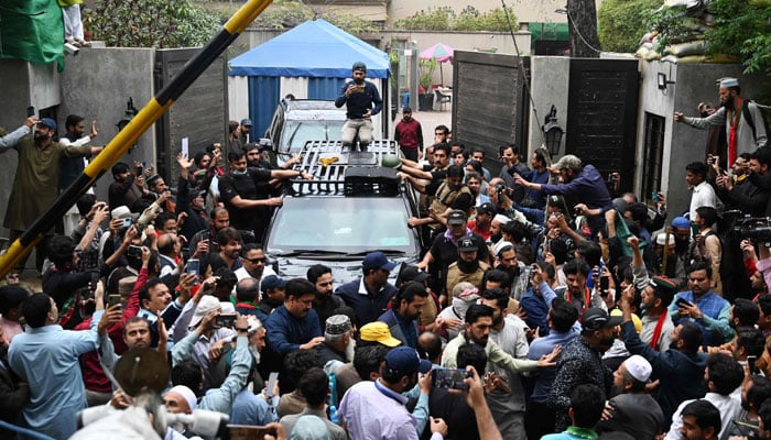 Supporters of former prime minister Imran Khan gather around his car as he leaves his residence in Lahore on March 18, 2023, on his way to appear in a court in Islamabad. — AFP