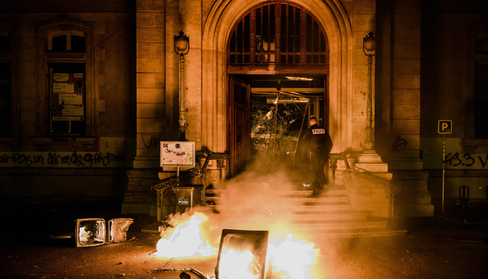 A police officer attempts to extinguish flames at the entrance of the town hall of the 4th arrondissement (district) of Lyon which was vandalised during riots following a demonstration on March 17, 2023, in Lyon. — AFP