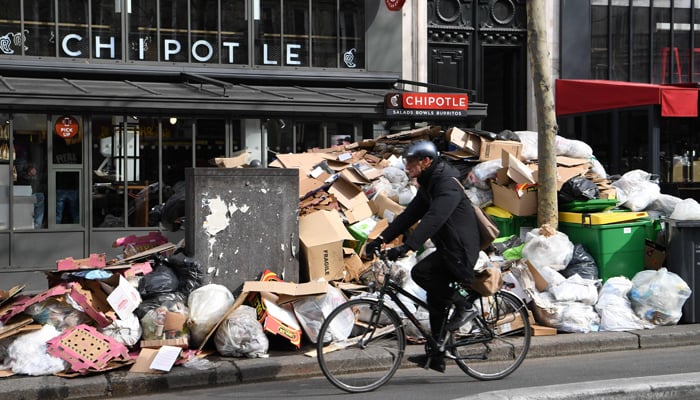 Man on a bicycle passes full waste bins in Paris as rubbish collectors strike against pension reforms, leaving many streets in the capital piled with stinking waste on March 17, 2023. — AFP