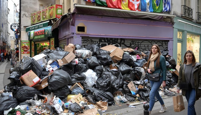 Pedestrians walk past full waste bins in Paris 5th district as rubbish collectors strike against pension reforms, leaving many streets in the capital piled with stinking waste on March 17, 2023. — AFP