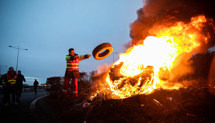 A person feeds a fire on a road in Le Havre, northwestern France, on March 21, 2023, as they block the industrial zone. — AFP