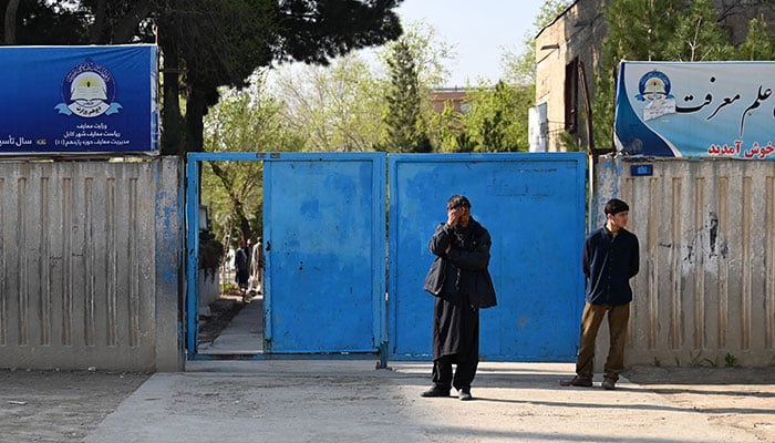 Afghan men stand at the entrance gate of a school in Kabul on March 21, 2023.— AFP