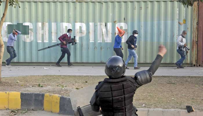 A police personal throwing stone on supporters of former Prime Minister Imran Khan, as media persons run and save themselves during clashes, between police and PTI workers, outside Judicial Complex in Islamabad on March 18, 2023. — ONLINE