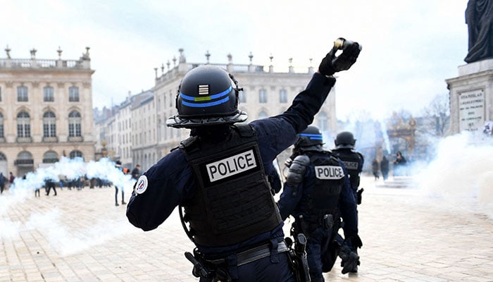 Police officer throws a smoke bomb at the Place Stanislas (Stanislas square) during a demonstration, a week after the government pushed a pensions reform through parliament without a vote, using the article 49.3 of the constitution, in Nancy, eastern France on March 23, 2023.—AFP