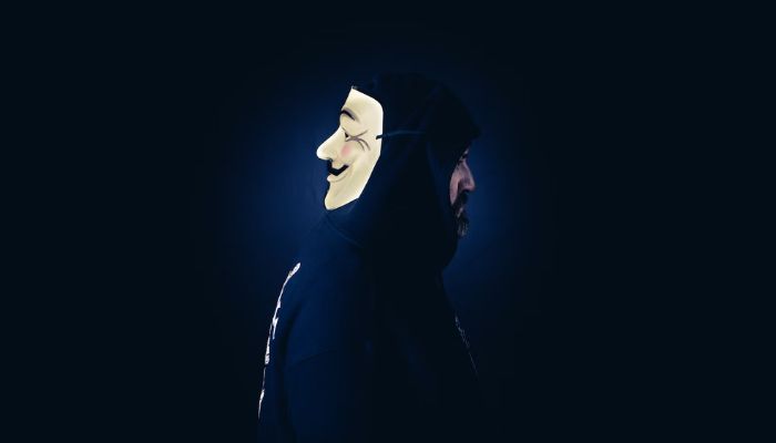 A man in a hoodie wears a Guy Fawkes mask on the back of head.— Unsplash