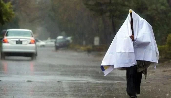 A man covers himself with a sheet while walking on the road during a rainy day. — AFP/File