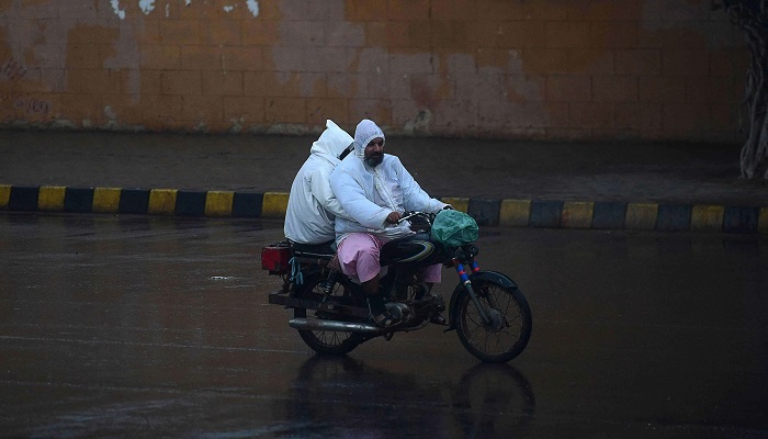 Commuters ride on a motorbike along a road during rainfall in Karachi. — AFP/ File