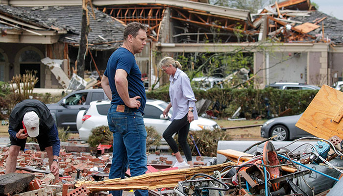 (FILES) In this file photo taken on March 31, 2023, Kris French (C) and his family search through rubble for a video recorder they think captured a direct tornado strike to their business. —AFP