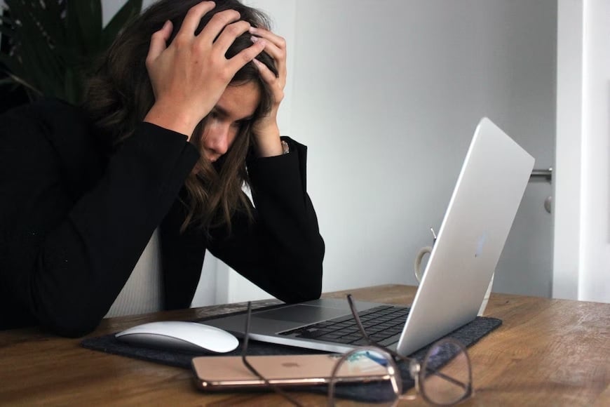 Image shows a stressed woman sitting in front of her laptop.— Unsplash