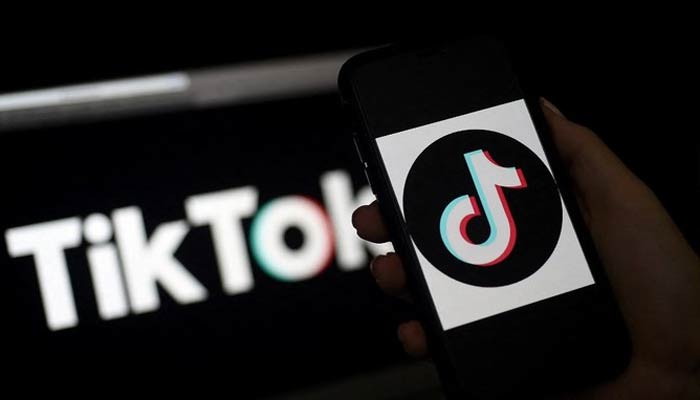 A person holds a phone showing TikTok logo against logo in the background. — AFP/Files