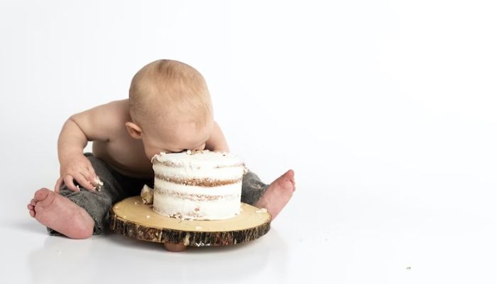 The image shows an infant trying to eat a cake.— Pexels